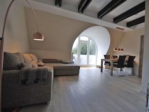 A modern loft with a large arched window, a sectional sofa, a dining area, and a pendant light.