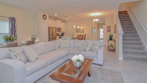A modern living room with a sectional sofa, a wooden coffee table, and a staircase leading to the upper floor. - Go 27 - Champions Gate (Kissimmee)