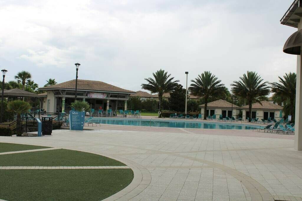 A pool area with lounge chairs, palm trees, and a building with a tiled roof.