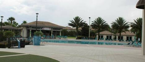 A pool area with lounge chairs, palm trees, and a building with a tiled roof.