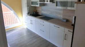 A kitchen with white cabinets, a black countertop, and a window with a view of a brick wall.