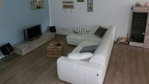 A living room with a white sofa, a television on a wooden stand, a small wooden table, and a cabinet with glass doors. - Stralsund Altstadt, 2-Zi-Wohnung mit Loggia (Stralsund)