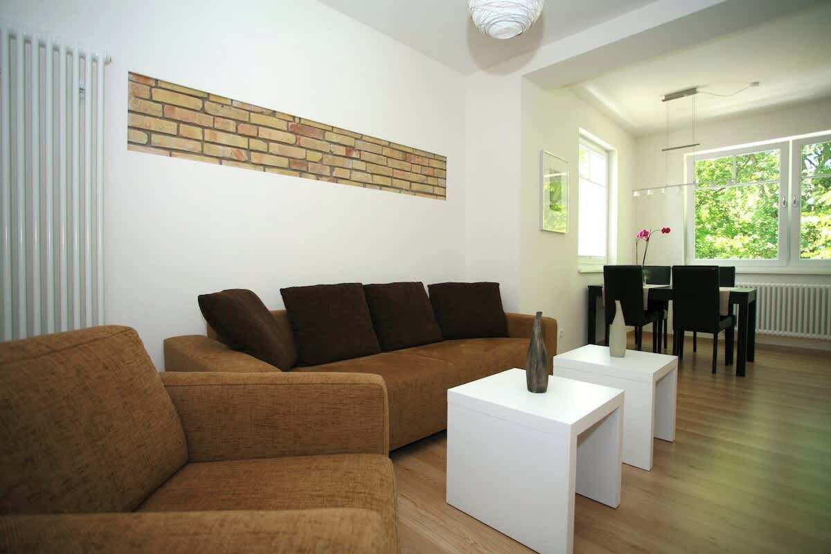 Un salón moderno con un sofá marrón, mesitas blancas y una pared de ladrillo decorativa.