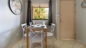 A dining area with a table set for four, white chairs, a window with curtains, and a door.