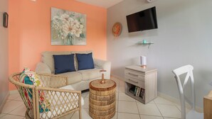 A living room with a sofa, a wicker chair, a round side table, a television, and a bookshelf.