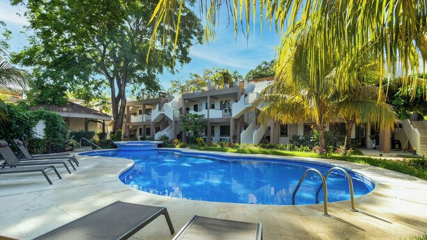 A swimming pool with lounge chairs, a covered deck, and a building with balconies.