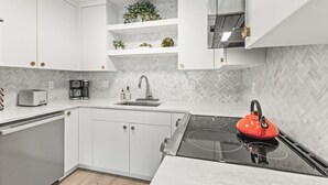 A modern kitchen with white cabinets, a herringbone-patterned backsplash, a gas stove, and a red kettle.