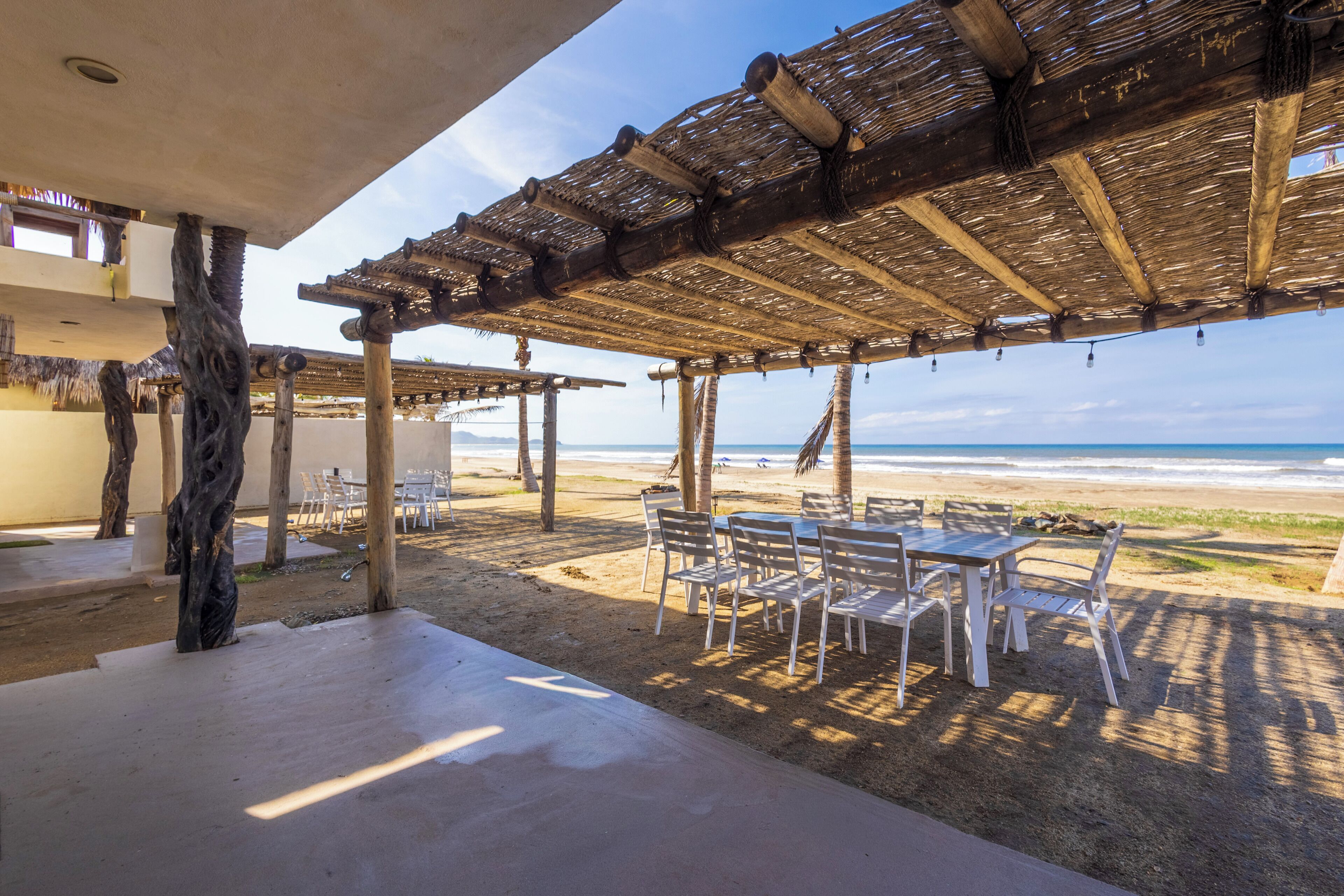 Un espacio de estar al aire libre con techo de paja, sillas blancas y vistas a la playa.