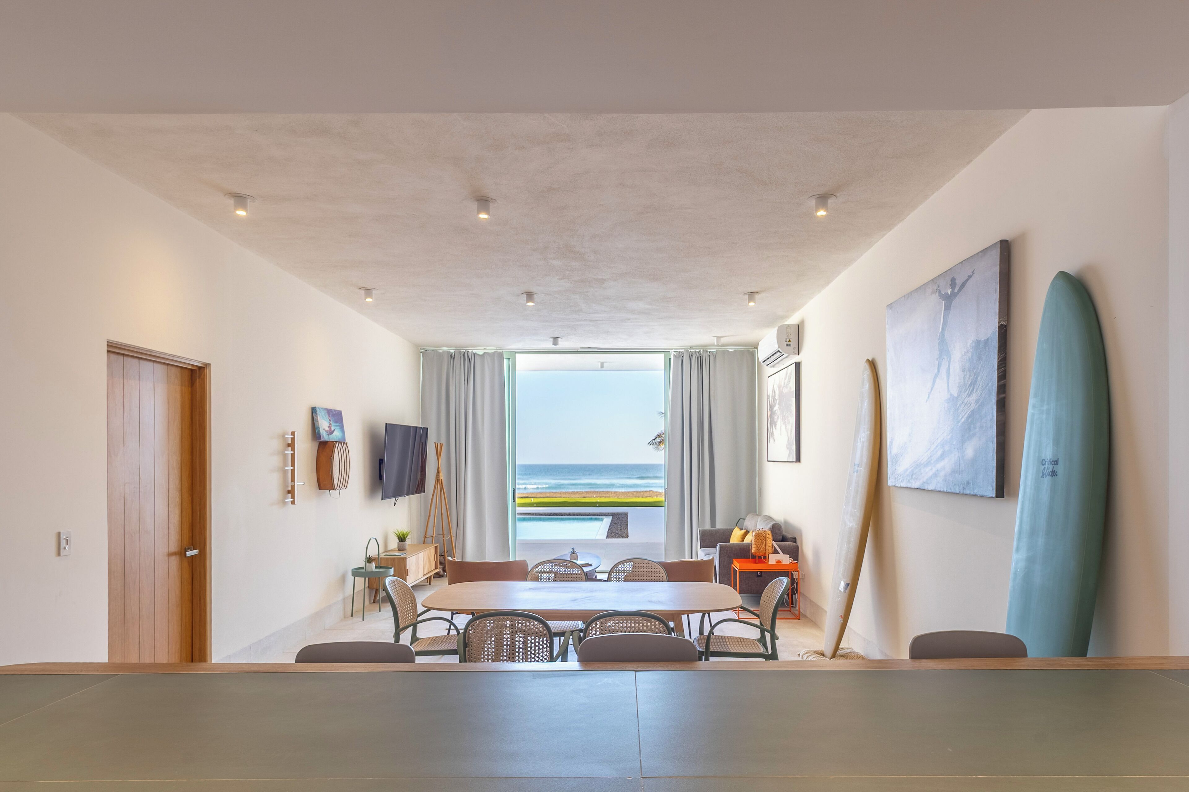 A spacious room with a large dining table, a view of the ocean, and surfboards on the wall.