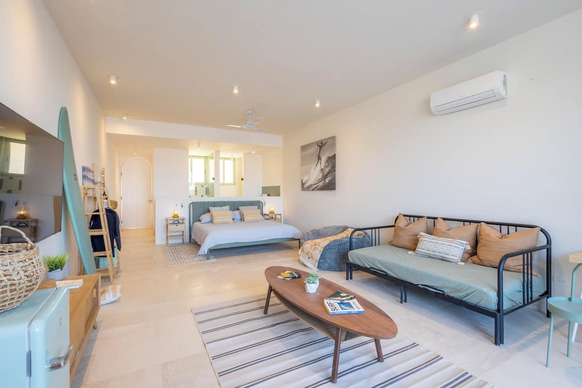 Una sala de estar moderna y bien iluminada con un sofá, una mesa de centro y una cama con vistas al dormitorio contiguo.