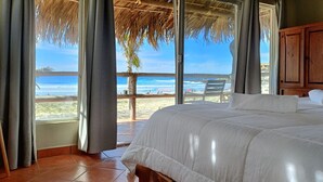A bedroom with a large bed, a wooden headboard, and a view of the beach and ocean through a glass door. - Costa Cerritos Beach Front Property (El Pescadero)