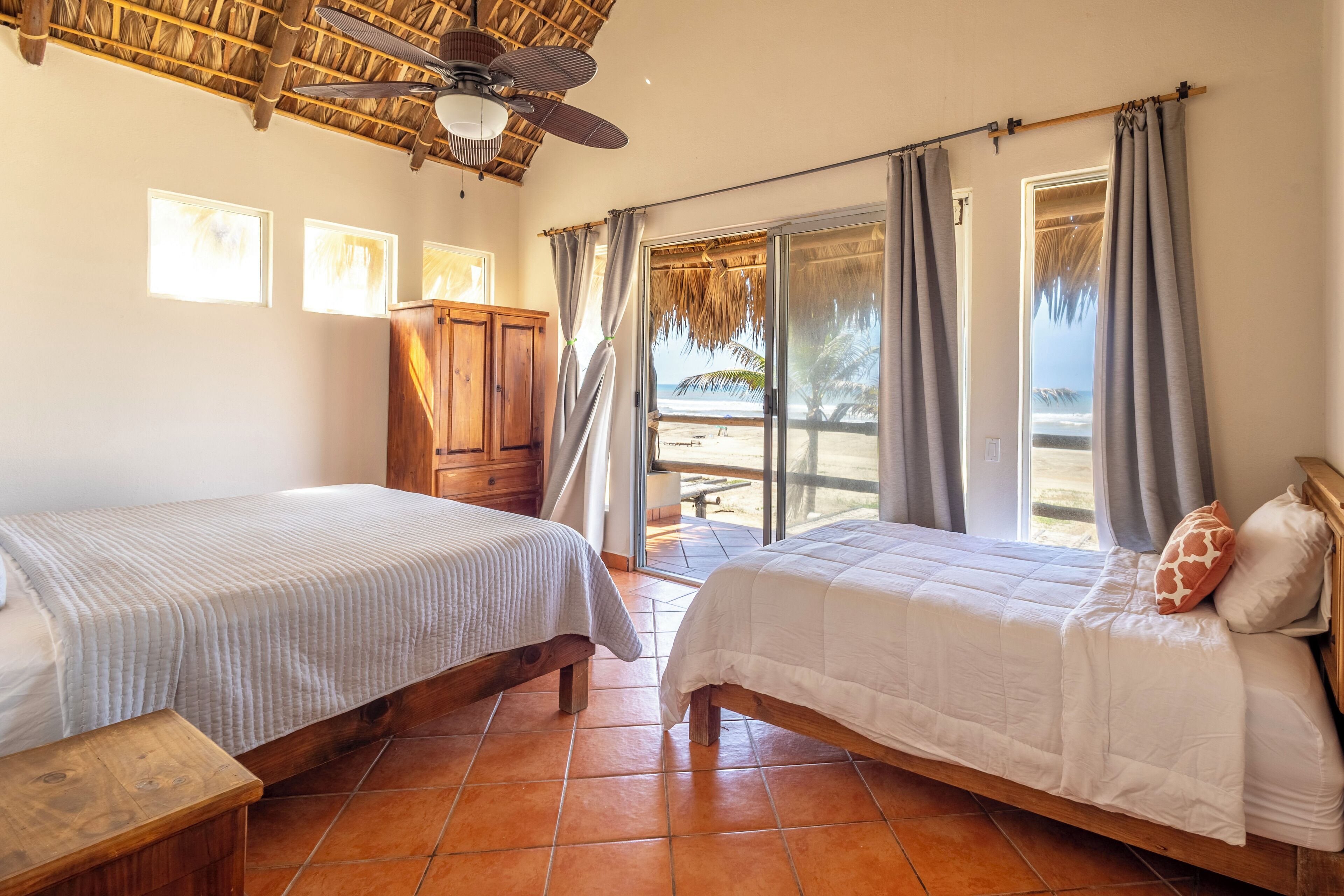Ein Zimmer mit zwei Betten, einem Holzschrank, einem Deckenventilator und Blick auf den Strand.