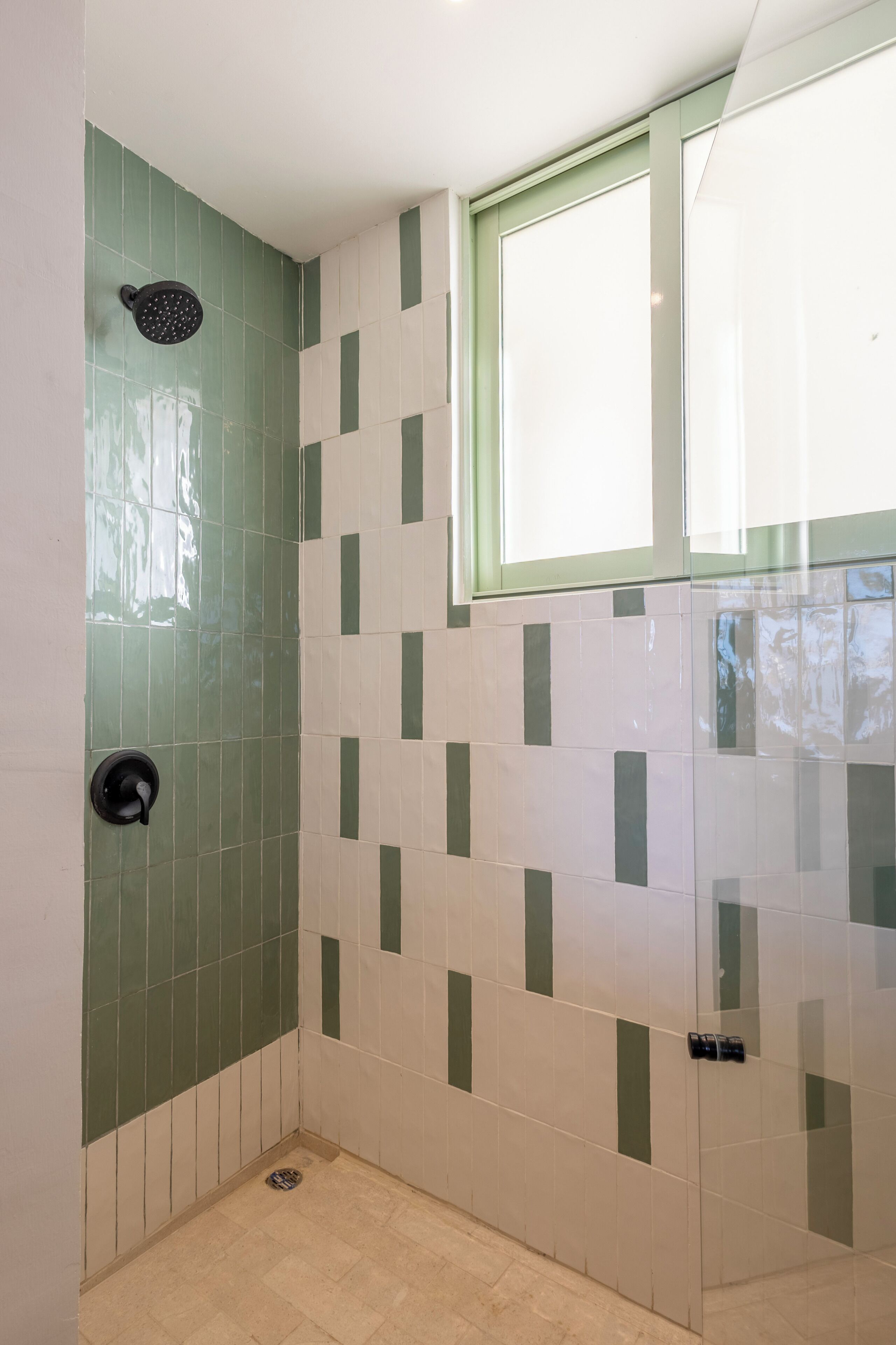 Un baño con ducha, ventana y pared de azulejos.