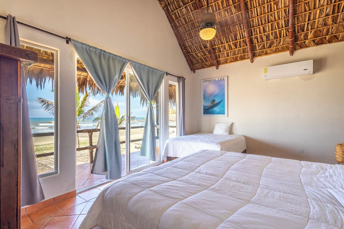 Una habitación con dos camas, vista a la playa, techo de paja y un cartel en la pared.