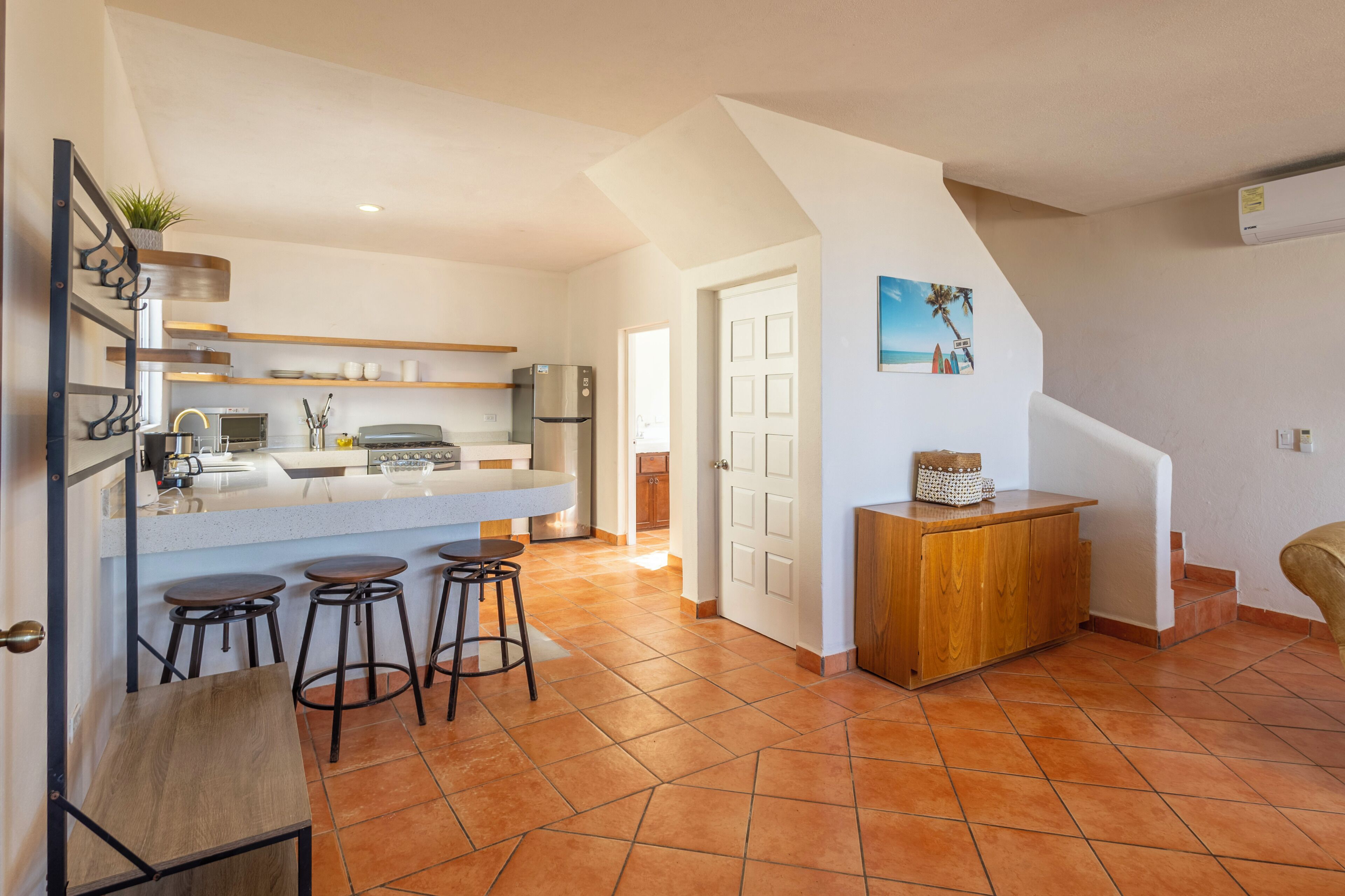 A modern kitchen with a central island, bar stools, and a wooden cabinet.