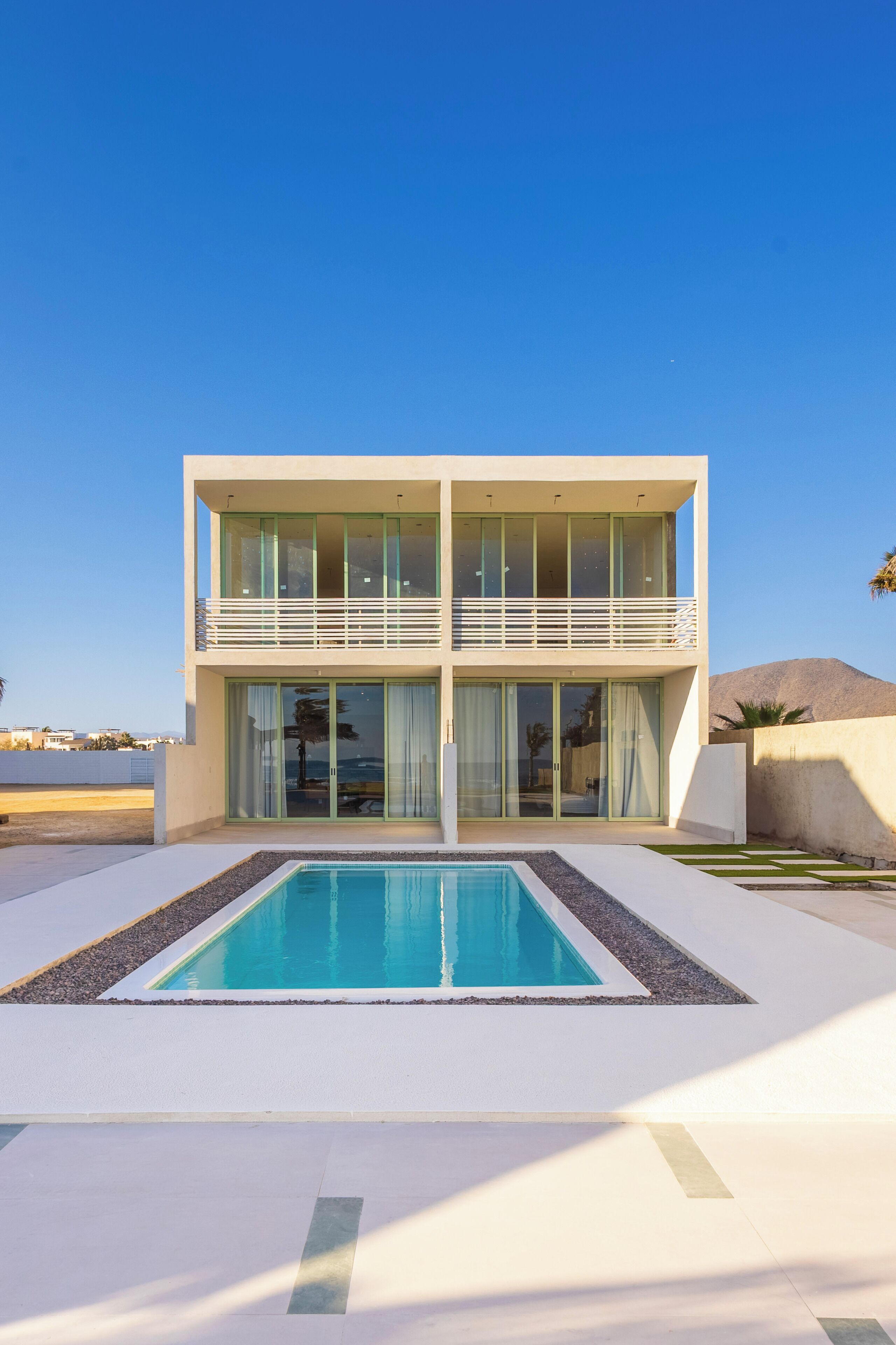 A modern two-story house with a large glass balcony, a swimming pool, and a view of the sea.