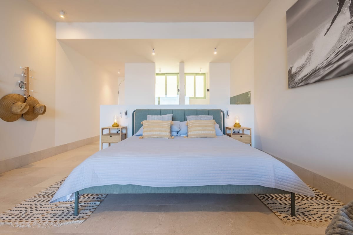 Un dormitorio moderno con una cama grande, dos mesitas de noche con lámparas, un cabecero y un ventanal con vistas.