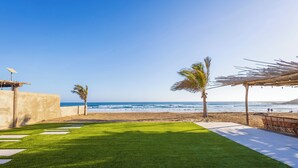A beach view with a grassy area, palm trees, and a wooden pergola. - Costa Cerritos Beach Front Property (El Pescadero)