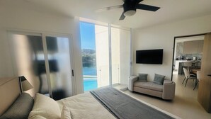Une chambre moderne avec un grand lit, un canapé, une télévision et un balcon offrant une vue sur l’eau.