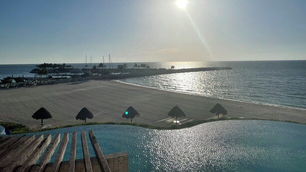 Un complexe hôtelier en bord de mer doté d’une piscine, de parasols en chaume et offrant une vue sur l’océan.