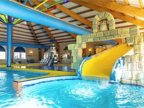 Una piscina interior con tobogán de agua, una estructura de juegos con forma de faro y un arco de piedra.