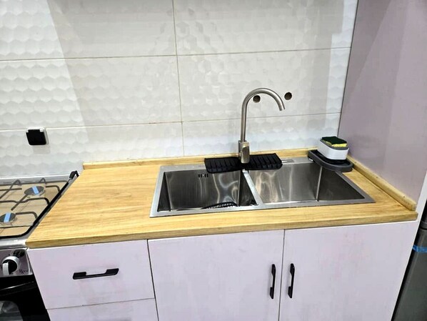 A kitchen with a stainless steel sink, wooden countertop, and white cabinets.