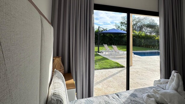 A bedroom with a large bed, a view of a swimming pool, and a staircase leading to an outdoor area.