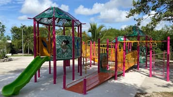 A playground with a green slide, climbing structures, and a covered play area.