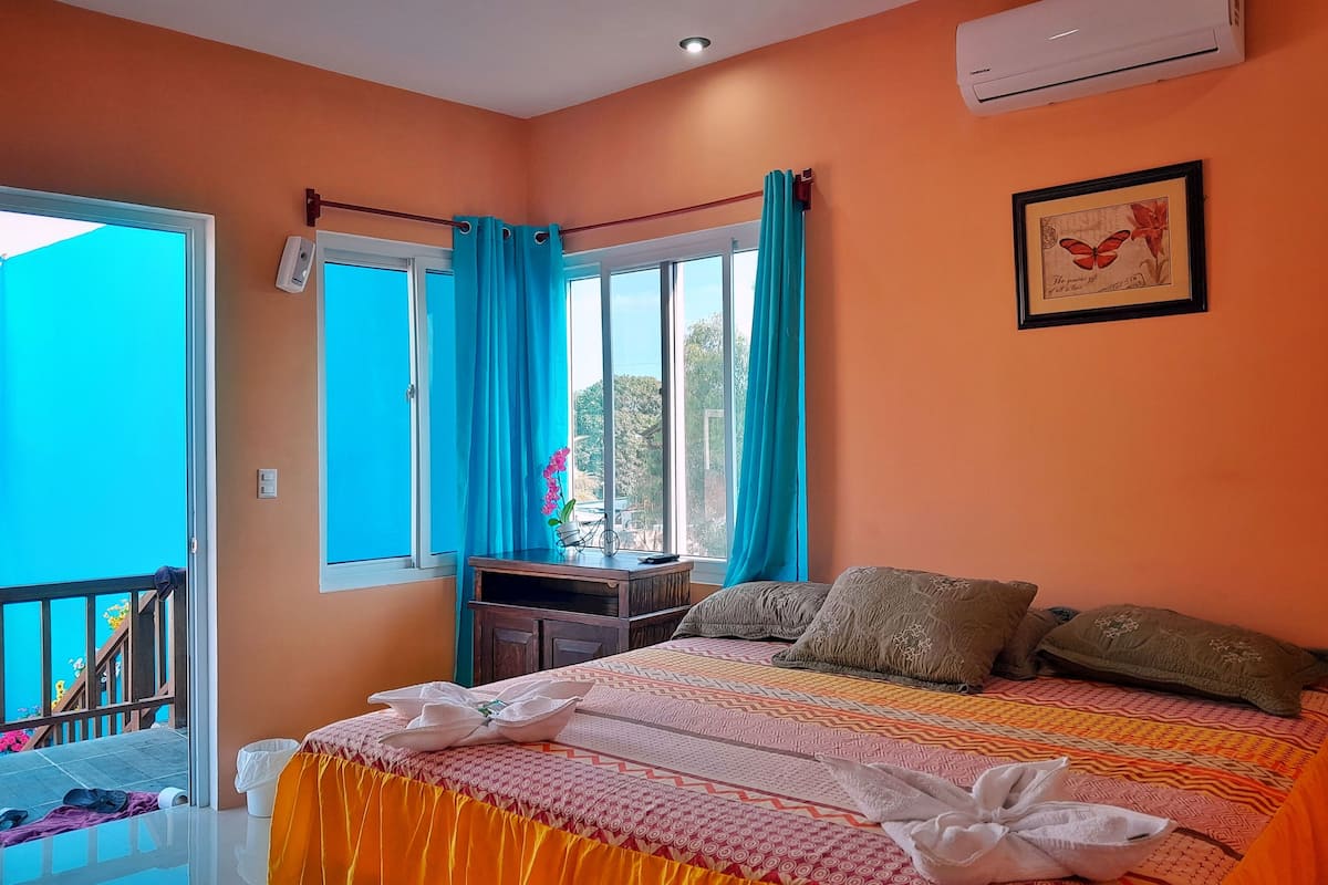 A bedroom with a bed, a window with curtains, a bedside table, and an air conditioner.