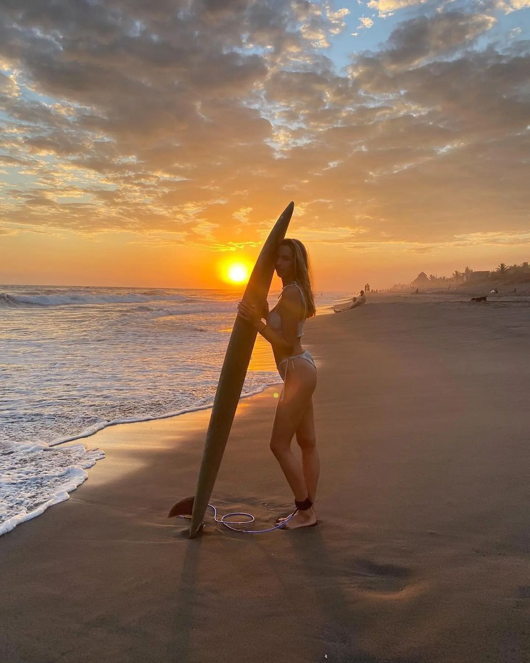 A person holding a surfboard on a beach at sunset.