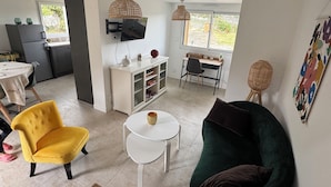 Un'ampia zona giorno con una poltrona gialla, un divano verde, un tavolino da caffè bianco e una TV montata a parete.
