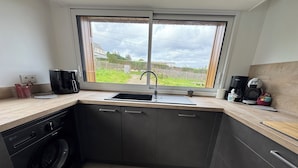 Una cucina compatta con lavatrice integrata, lavandino e finestra vista giardino.