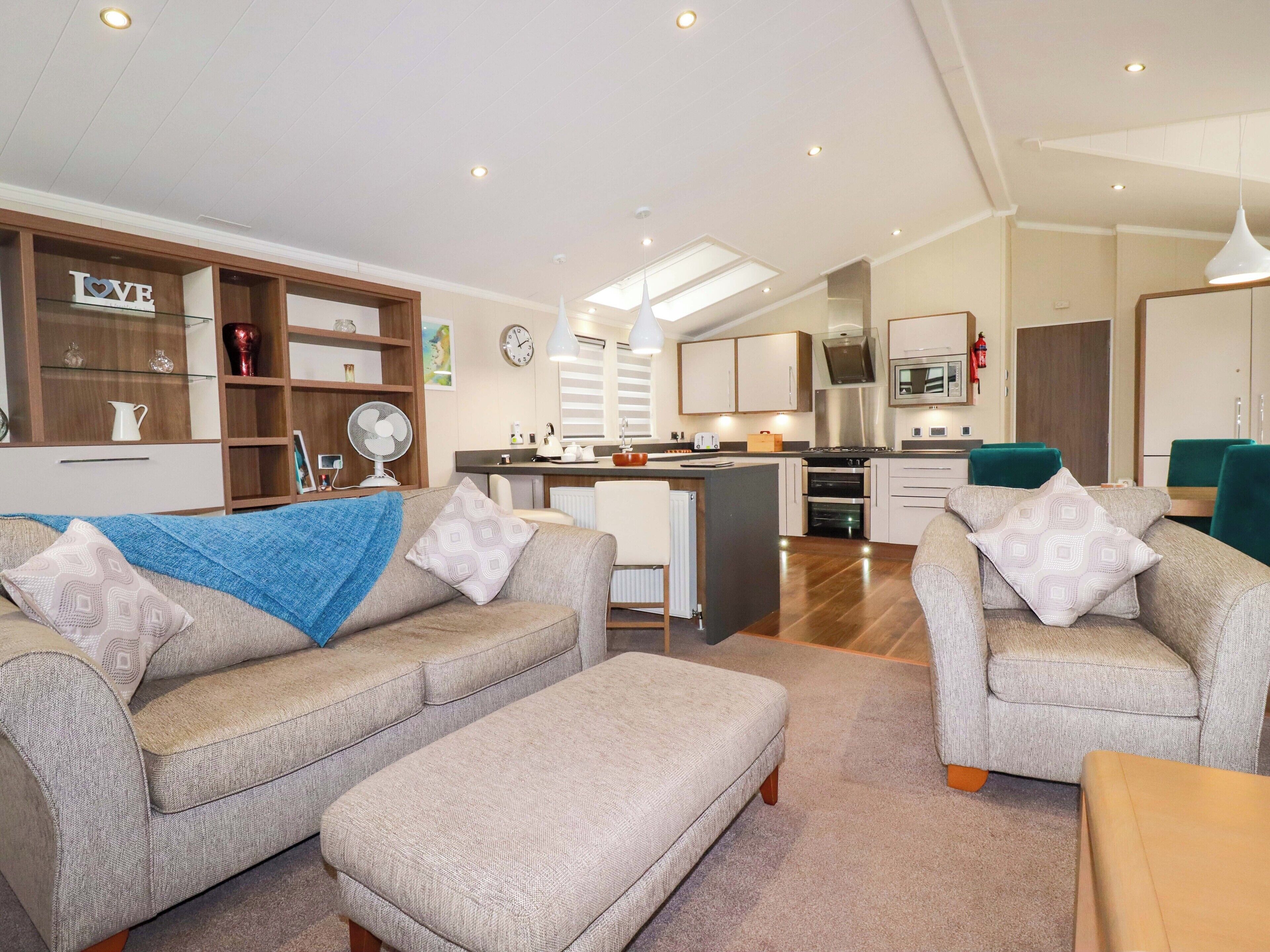 A modern living room with a sofa and ottoman, a kitchen with a central island, and a dining area with chairs.