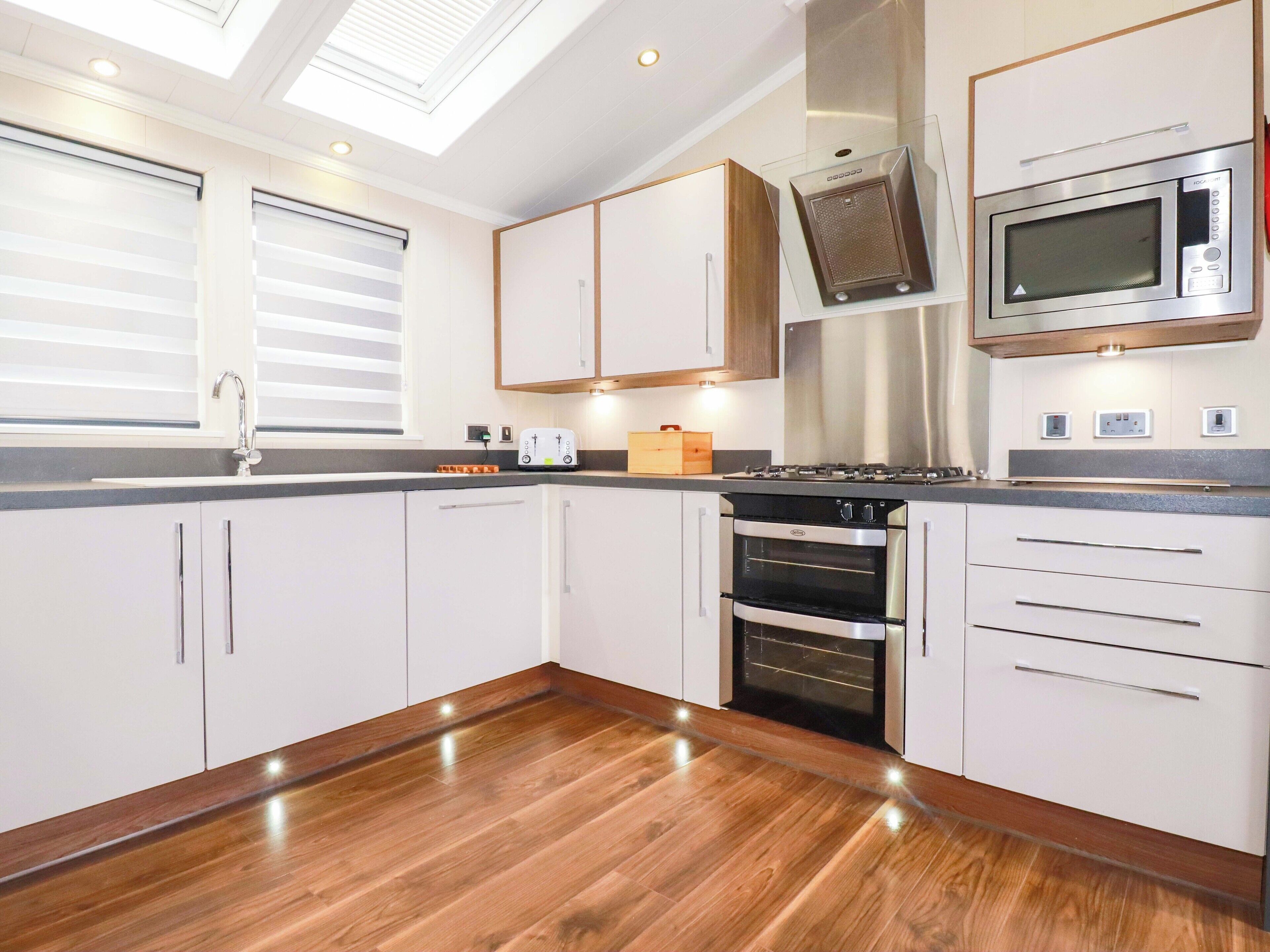 A modern kitchen with white cabinets, a stainless steel microwave, a built-in oven, and a skylight.