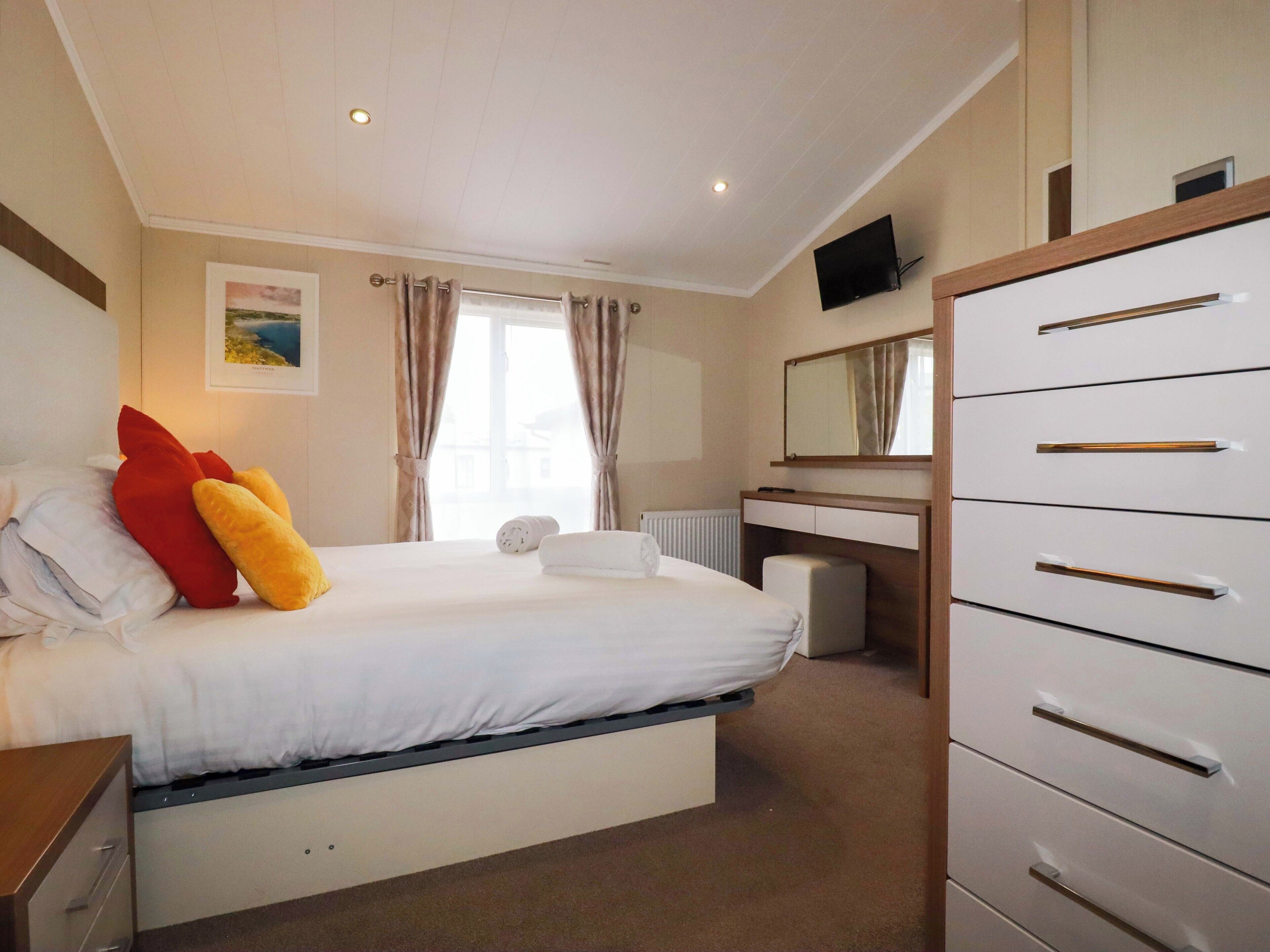 A hotel room with a bed, a desk, a dresser, a television, and a window with curtains.