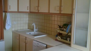 A kitchen with beige cabinets, a white sink, and a tiled backsplash. - ΜΟΝΟΚΑΤΟΙΚΙΑ ΣΕ ΠΑΡΑΔΟΣΙΑΚΟ ΟΙΚΙΣΜΟ (ΜΥΡΙΝΑ ΛΗΜΝΟΥ)