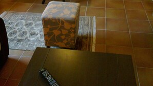 A dining area with a table and four patterned chairs, a small ottoman, and a remote control on a table. - ΜΟΝΟΚΑΤΟΙΚΙΑ ΣΕ ΠΑΡΑΔΟΣΙΑΚΟ ΟΙΚΙΣΜΟ (ΜΥΡΙΝΑ ΛΗΜΝΟΥ)