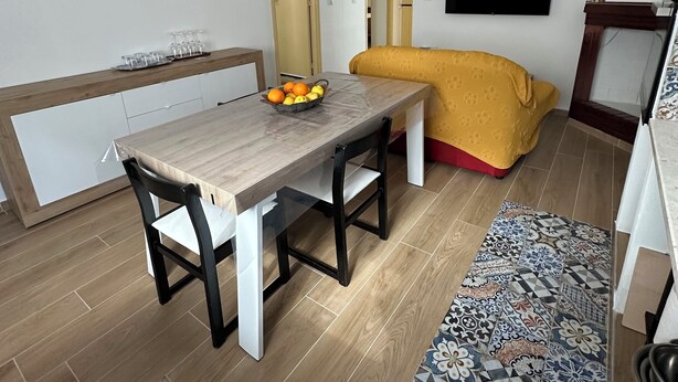 Een moderne woonkamer met een houten eettafel, een bank, een aan de muur bevestigde televisie en een kamerkleed met een patroon.