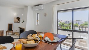 Ein modernes Wohnzimmer mit Essbereich, Kamin und großem Fenster mit Blick auf Gebäude.