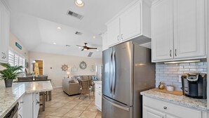 A modern kitchen with white cabinetry, a stainless steel refrigerator, and a coffee maker on the counter. - Purple Pelican Paradise by Ryson Vacation Rentals (Galveston)