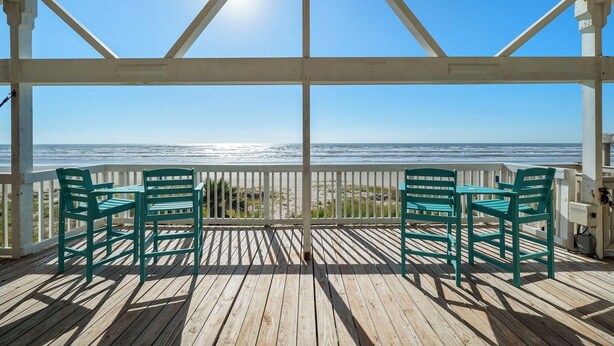 A covered outdoor area with two green chairs facing a beach view. - Parijatha by Ryson Vacation Rentals (Galveston)