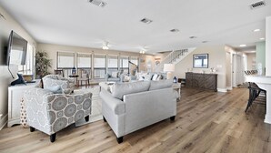A spacious living room with a large grey sofa, a patterned armchair, and a wooden floor.
