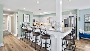 A modern kitchen with a central island, bar stools, and a blue sofa by the window.