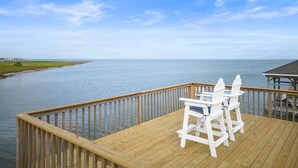 A wooden deck with two white Adirondack chairs overlooking a calm body of water and a distant shoreline.