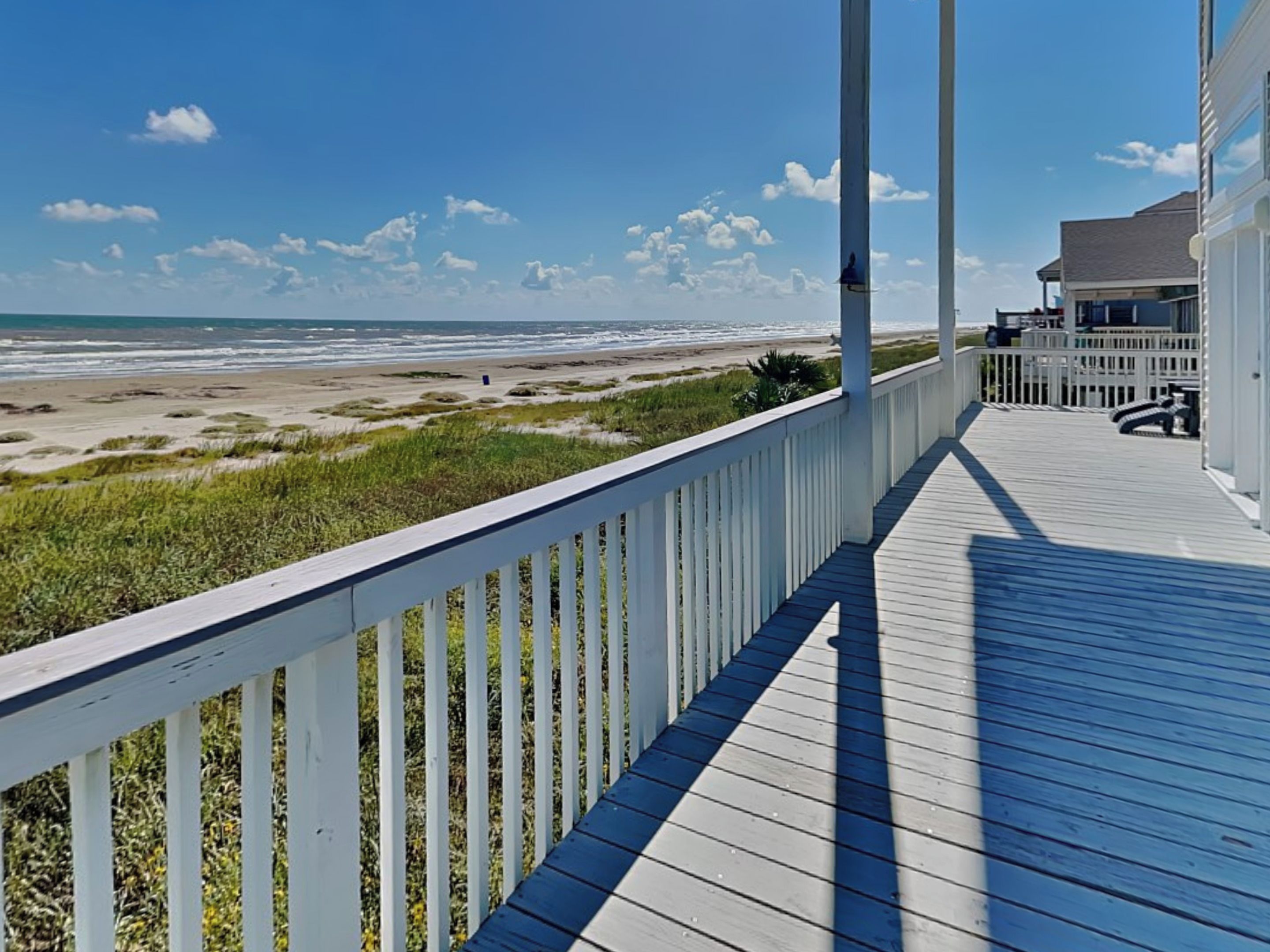 Eine Holzterrasse mit Blick auf Strand und Meer.