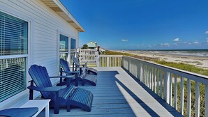 A wooden deck with Adirondack chairs, a white railing, and a view of the beach. - Casablanca by Ryson Vacation Rentals (Galveston)