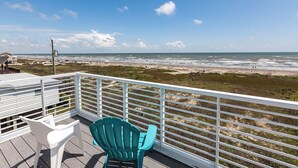 A deck with a white railing, a turquoise chair, and a white table. - Beachfront Melody by Ryson Vacation Rentals (Galveston)