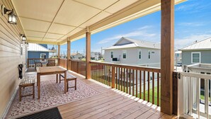 A covered outdoor deck with a wooden table and chairs, a railing, and a view of neighboring houses. - Copper Top by Ryson Vacation Rentals (Galveston)