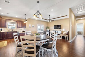 Une cuisine moderne avec des meubles en bois foncé, un coin repas avec des chaises blanches, un ventilateur de plafond et une grande fenêtre.