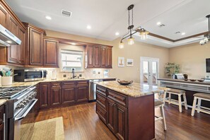 A spacious kitchen with wooden cabinets, a granite countertop, and a large island with stools. - Copper Top by Ryson Vacation Rentals (Galveston)